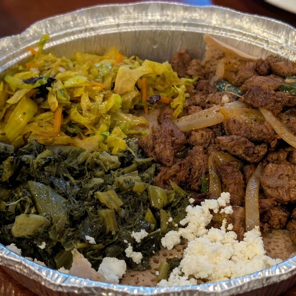 Aluminum tray filled with seasoned meat, sautéed cabbage, leafy greens, onions, peppers, and crumbled white cheese.